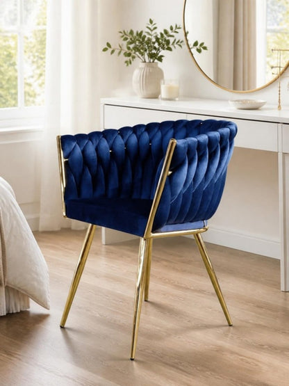 Silla de tocador de terciopelo azul con respaldo trenzado y patas doradas frente a un tocador blanco con espejo redondo en una recámara luminosa
